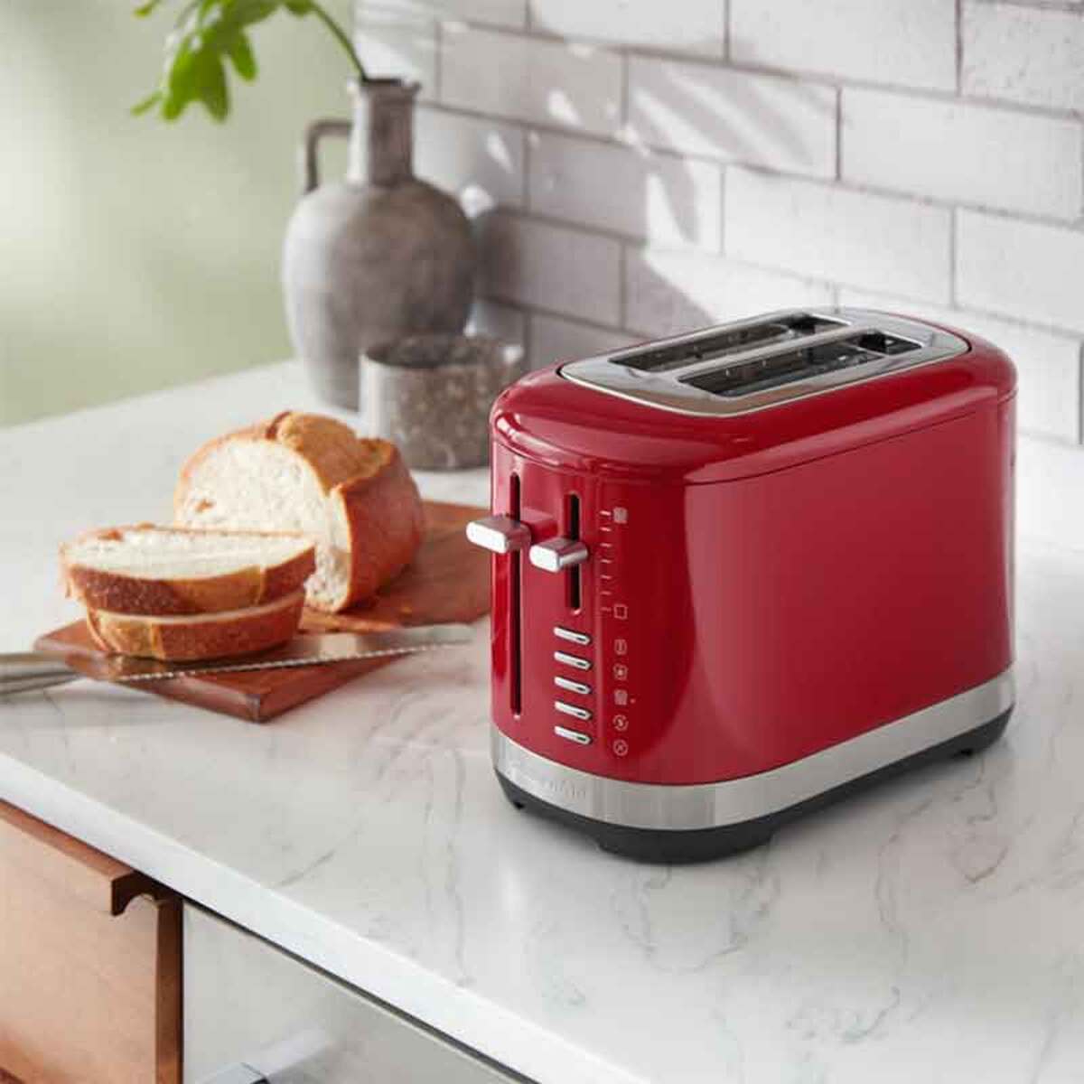 Bright empire red KitchenAid 5KMT2109BER manual control 2-slice toaster with silver accents, featuring two slots and adjustable settings, placed beside sliced bread on a marble countertop.