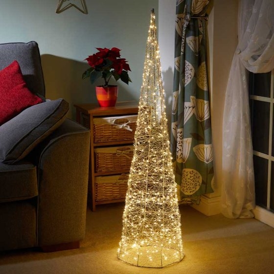 A tall, conical tree-shaped decoration made of intertwined golden LED lights, standing on a carpet beside a sofa and a potted poinsettia plant.