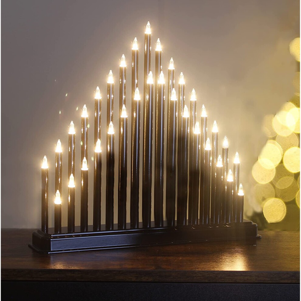 Black Candle Bridge featuring 33 faux candles arranged in a traditional triangular design, with warm white lights atop each candle, set against a blurred golden background.