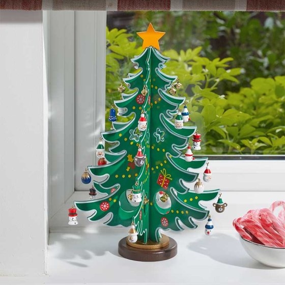 A vibrant green metal Christmas tree with a golden star on top, adorned with colorful ornaments and decorations, set on a wooden base near a window.