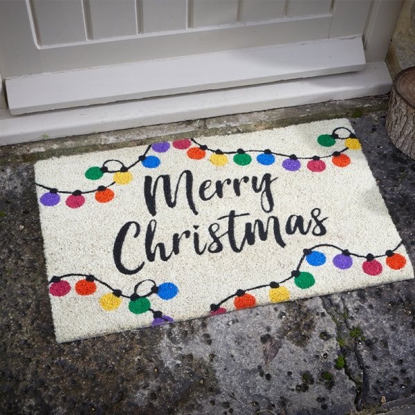 A festive doormat featuring "Merry Christmas" in bold black letters, adorned with colorful string lights on a textured, light-colored background, measuring 40x60cm.