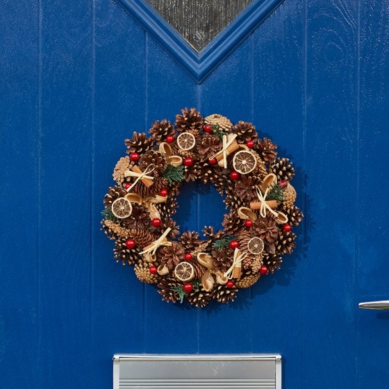 A 36cm winter spice wreath featuring natural pinecones, dried orange slices, red berries, and cinnamon sticks, set against a blue door.