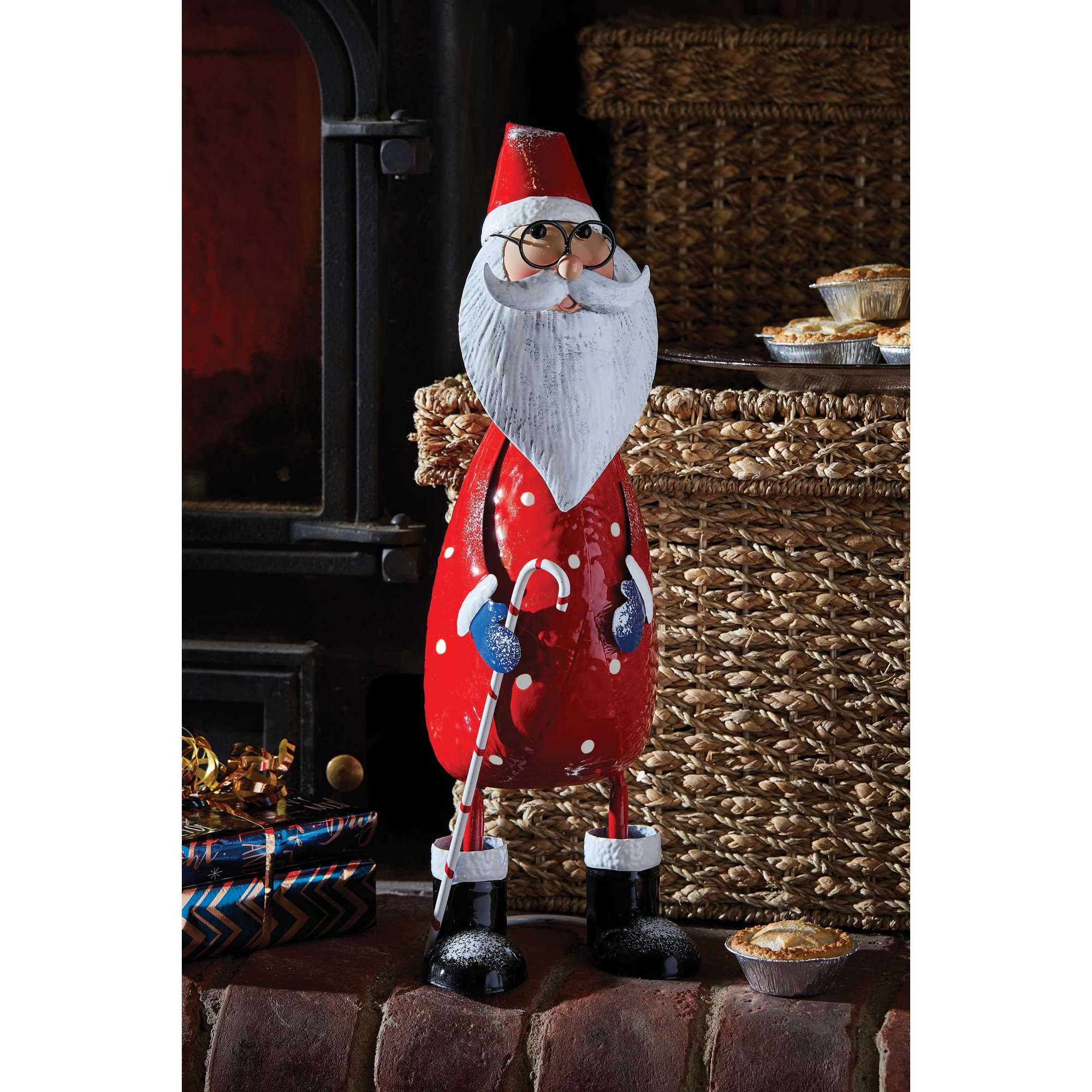 A whimsical red and white polka-dotted Santa figure with a long beard, glasses, and a red hat, made of metal, standing on a black base, surrounded by festive decor.
