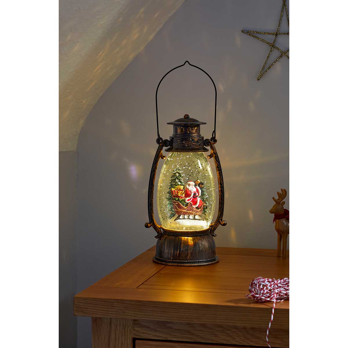 A decorative lantern featuring Santa Claus holding a gift, with a snow swirl effect, set against a warm amber glow, crafted from metal with a rustic finish.