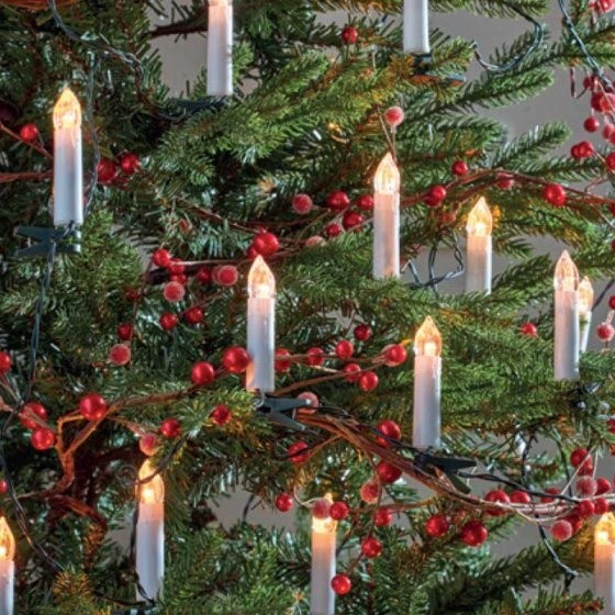 Warm white candle string lights with 50 bulbs, featuring white candle-like designs, set against a backdrop of green foliage and red berries, creating a festive ambiance.