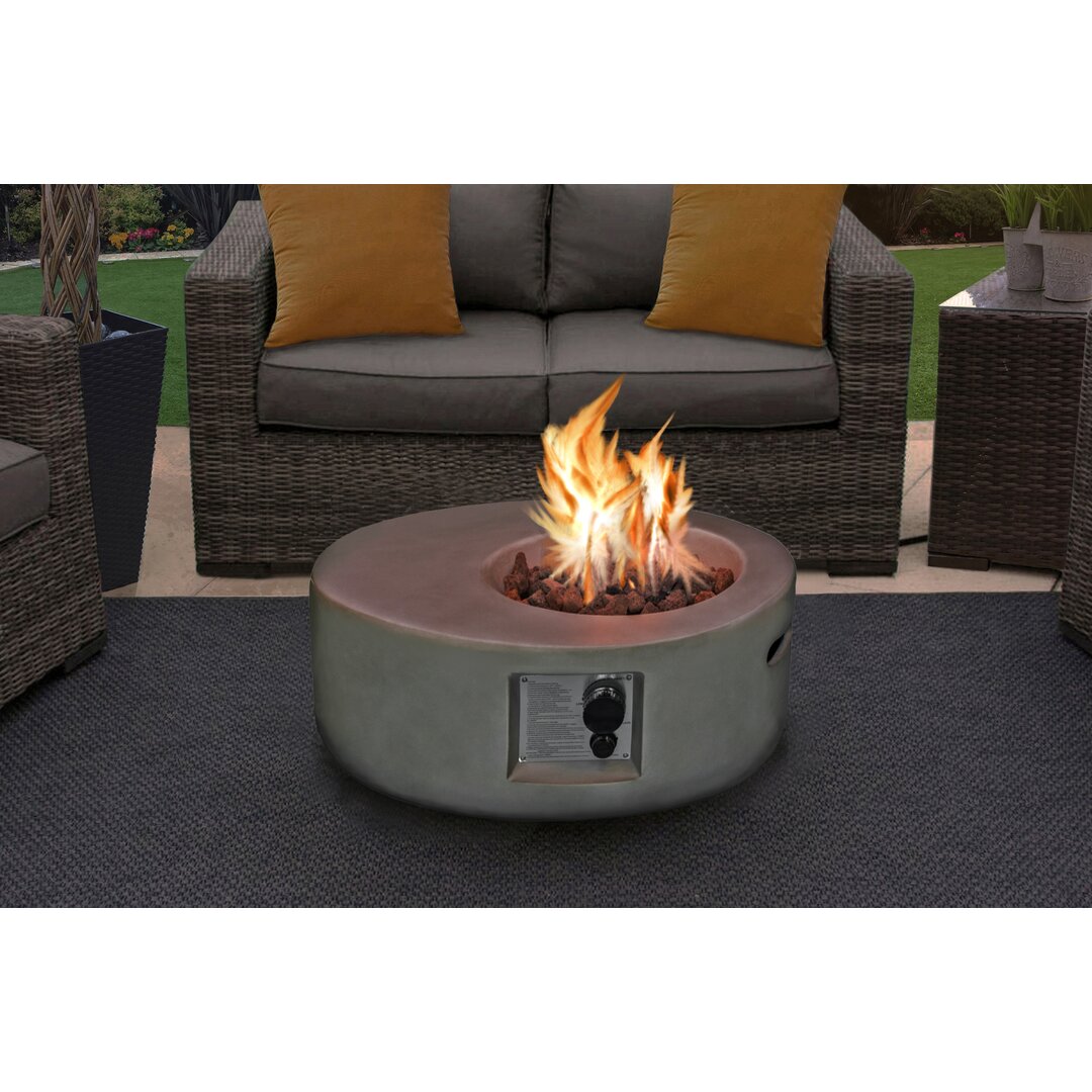 Round, gray concrete fire pit with a central flame, surrounded by decorative rocks, set on a patio with wicker furniture and cushions in a cozy outdoor living space.