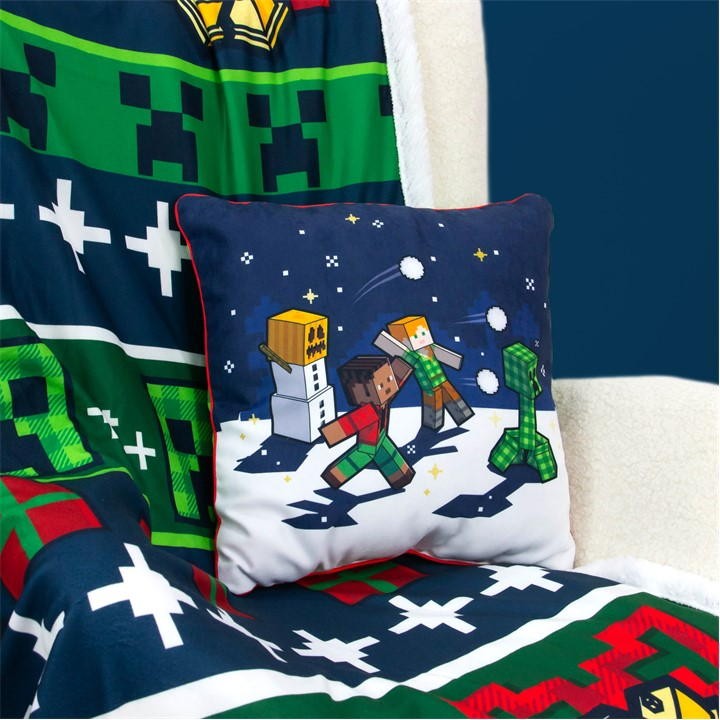 Minecraft Christmas cushion featuring colorful pixelated characters playing in the snow, with a blue background and red piping, made from soft fabric.