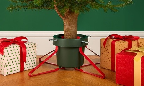 Green Christmas tree stand with a water reservoir, featuring red metal support arms, securely holding a tree, surrounded by wrapped gifts in festive colors.