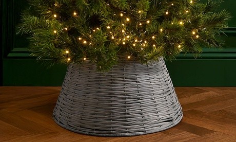 Gray woven tree skirt made of natural material, featuring a wide, flared design that complements a decorated Christmas tree with warm fairy lights.