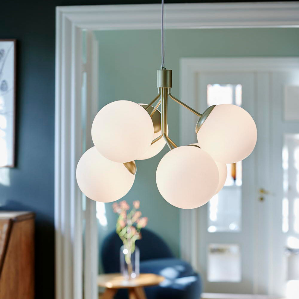 Brass pendant light featuring six spherical white glass shades arranged in a modern design, suspended from a sleek cord in a stylish interior setting.