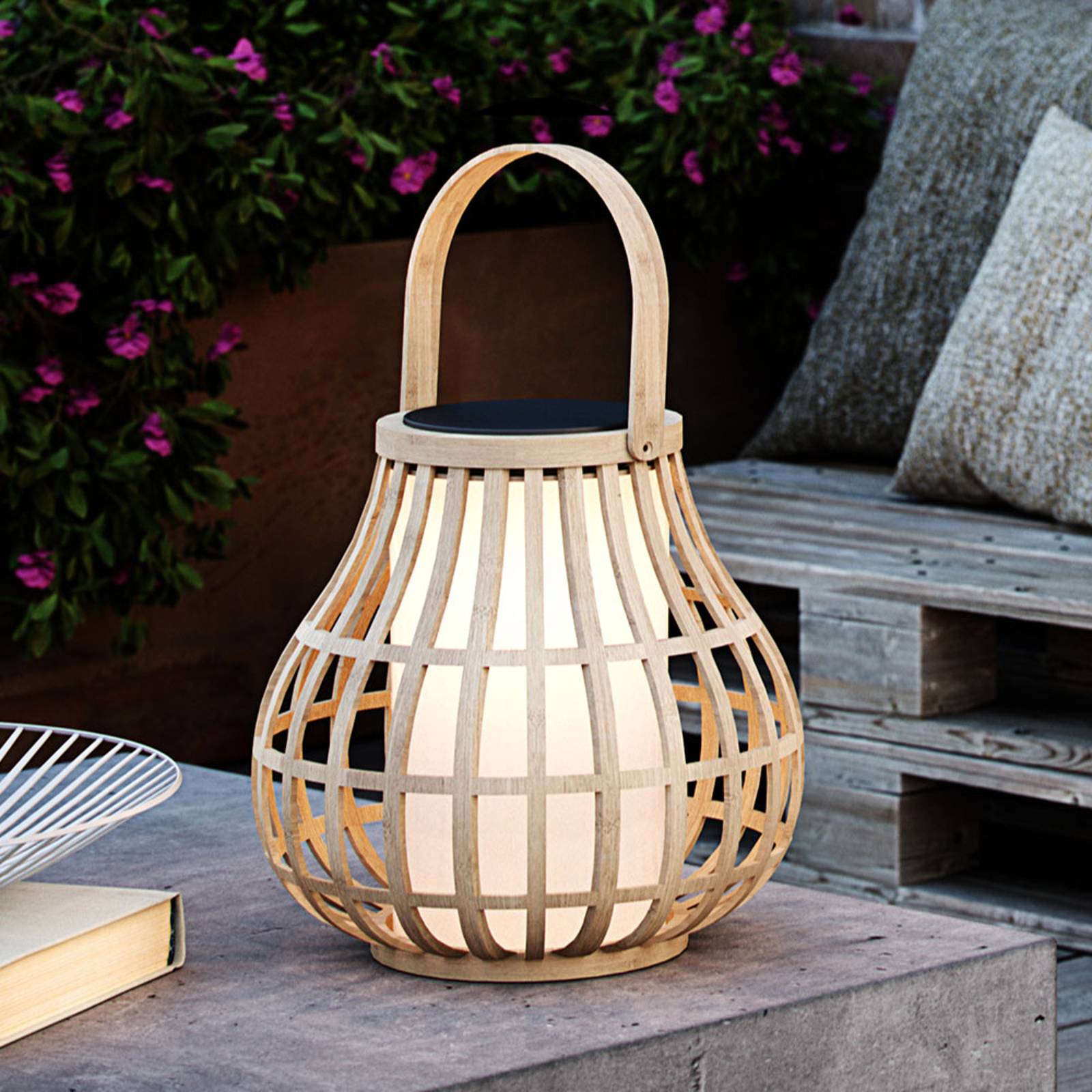 Bamboo lantern with a woven design, featuring a solar panel on top and a soft white light inside, placed on a wooden surface with greenery in the background.