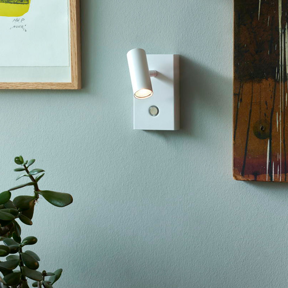 White wall light with a cylindrical shade, mounted on a rectangular base, featuring a sleek design, complemented by a small round switch, against a soft green wall.