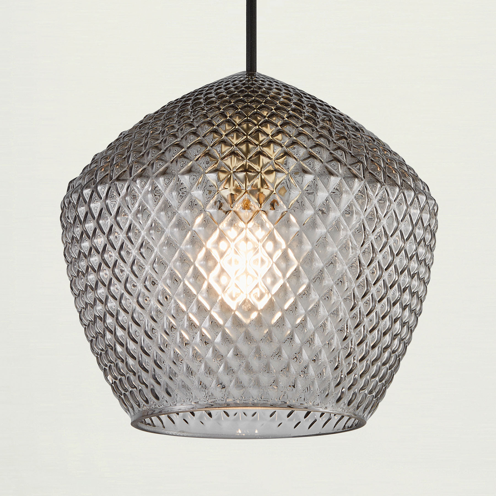 Grey pendant light with a textured, diamond-patterned glass shade and a warm glow from the interior bulb, suspended by a black cord.