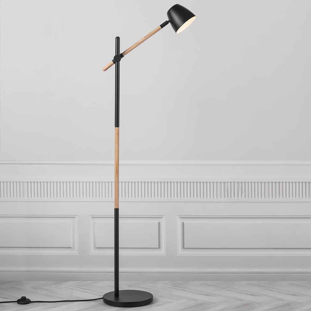 A sleek black floor lamp with a wooden accent, featuring an adjustable arm and a conical shade, set against a neutral wall with decorative molding.