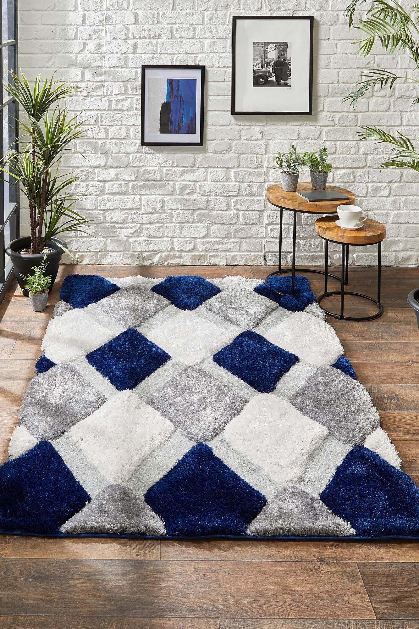 Soft shaggy rug featuring a geometric pattern in navy blue, gray, and white, with plush texture, set against a wooden floor and surrounded by potted plants and wall art.
