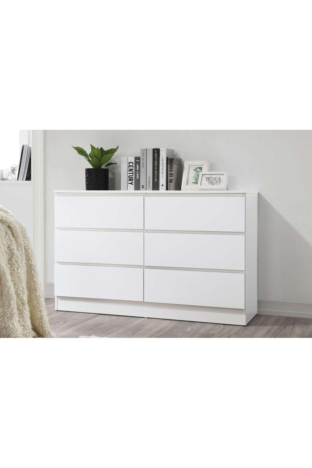 Birlea Oslo 6 Drawer Chest features a sleek white finish, six spacious drawers with minimalist handles, and a modern design, set against a light wood floor and decorated with books and a plant.