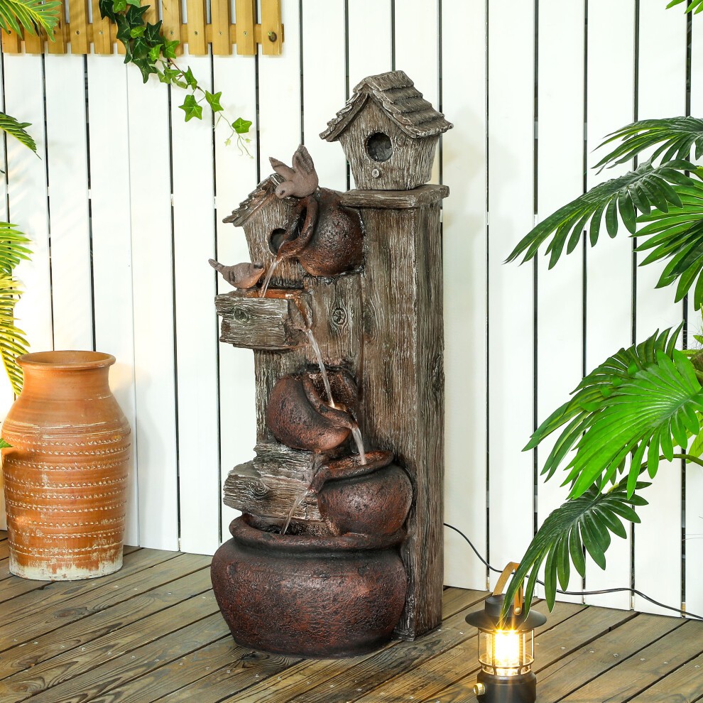Brown resin 2-in-1 waterfall fountain featuring a birdhouse, with cascading water flowing over textured logs into a round base, set against a wooden backdrop and surrounded by greenery.