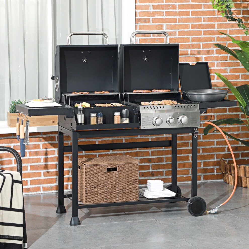 Black dual fuel BBQ grill with wheels, stainless steel burners, warming rack, and side shelves, set against a brick wall with greenery in the background.