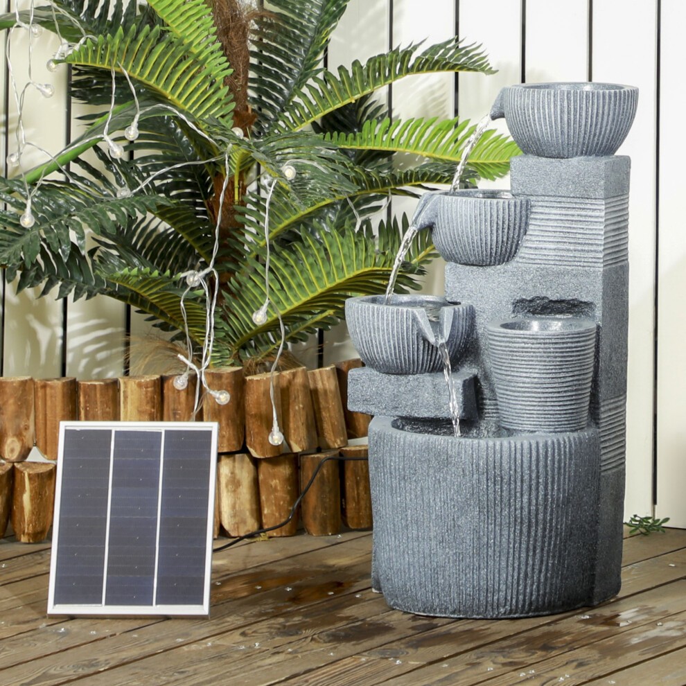 Gray stone-like outdoor waterfall fountain with multiple tiers, LED lights, and a solar panel, surrounded by greenery and wooden logs.