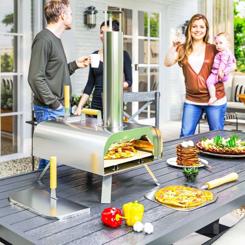 Portable silver wood pellet pizza oven with foldable legs, 12-inch stone, and wooden handles, set on a table with people enjoying a meal outdoors.