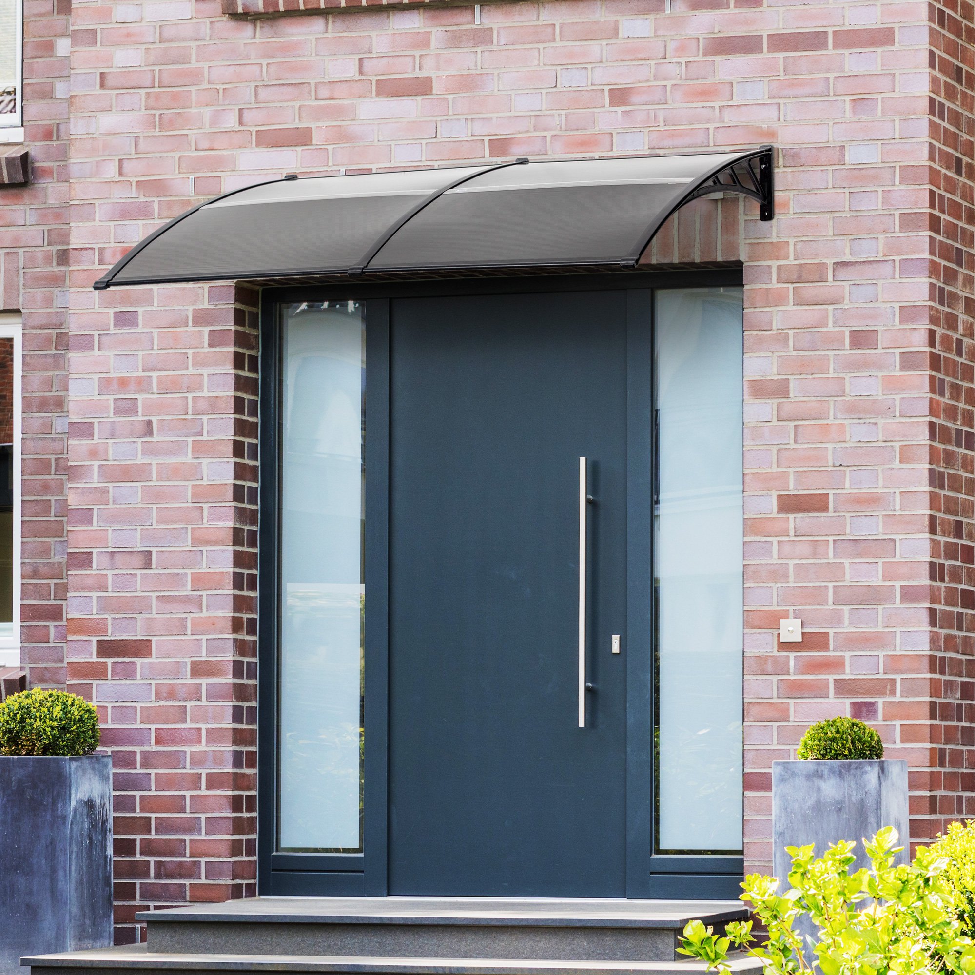 Black canopy measuring 200cm x 75cm, made of durable material, elegantly arches over a modern doorway, enhancing protection and style against the brick wall backdrop.