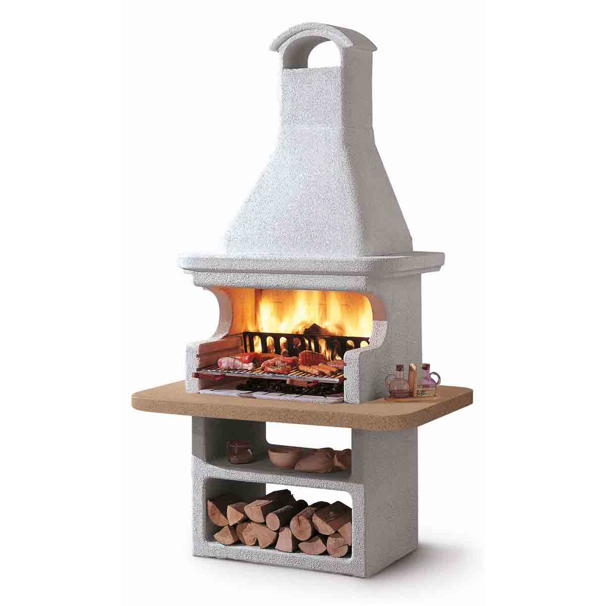 White masonry BBQ with a tall chimney, stone construction, a wooden shelf for prep, and an open fire area displaying grilling meat and logs underneath.