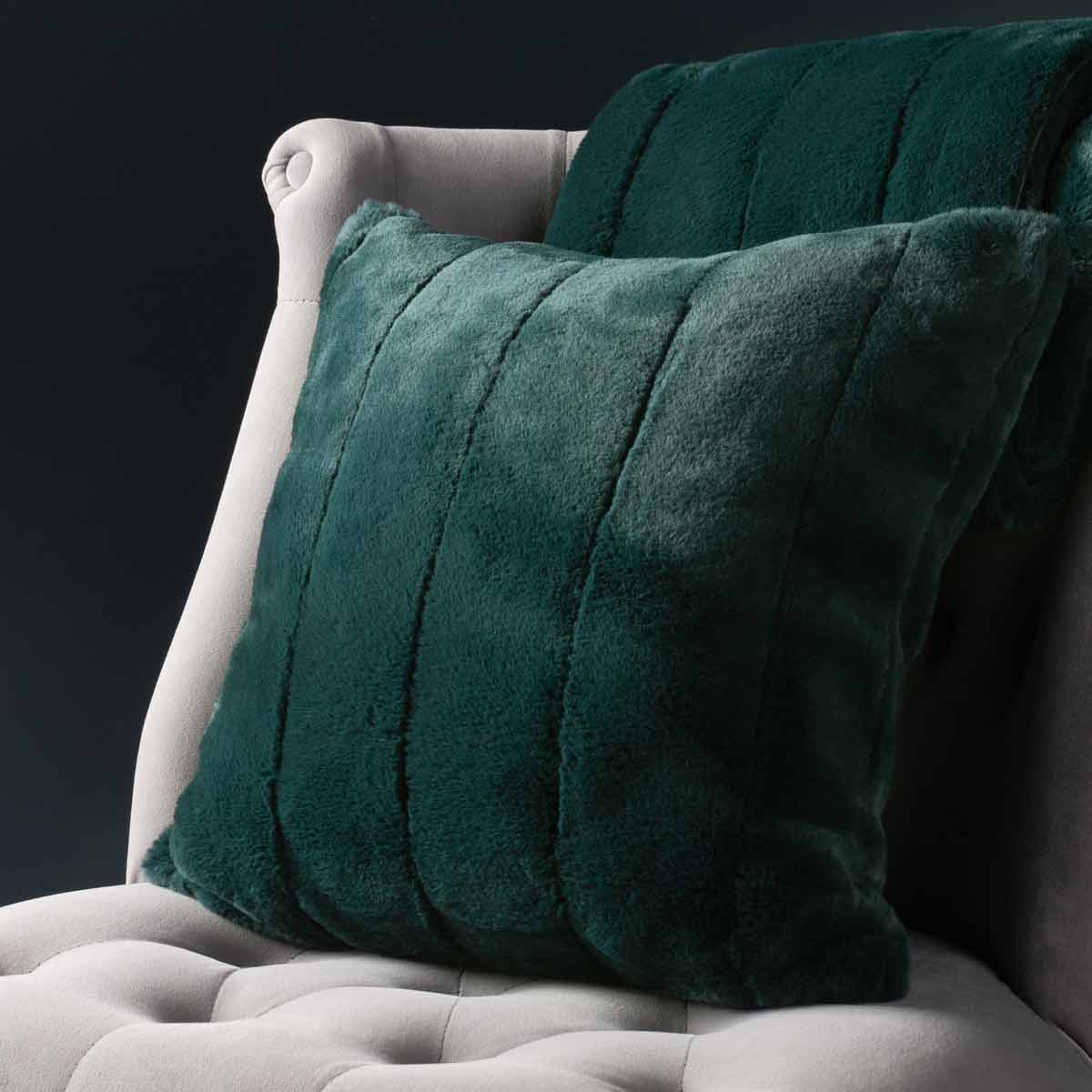 Emerald green faux fur cushion with a soft, plush texture, featuring vertical stripes, measuring 45cm x 45cm, placed on a light-colored upholstered chair.