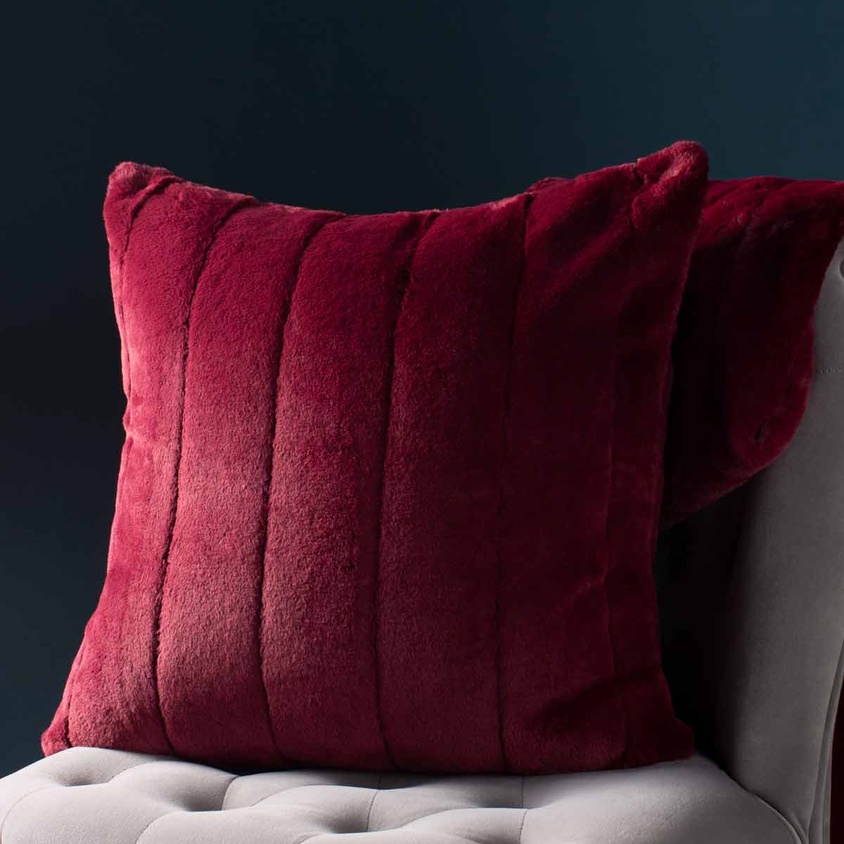Red faux fur cushion with vertical stripes, measuring 55cm x 55cm, featuring a plush texture, set against a dark background.