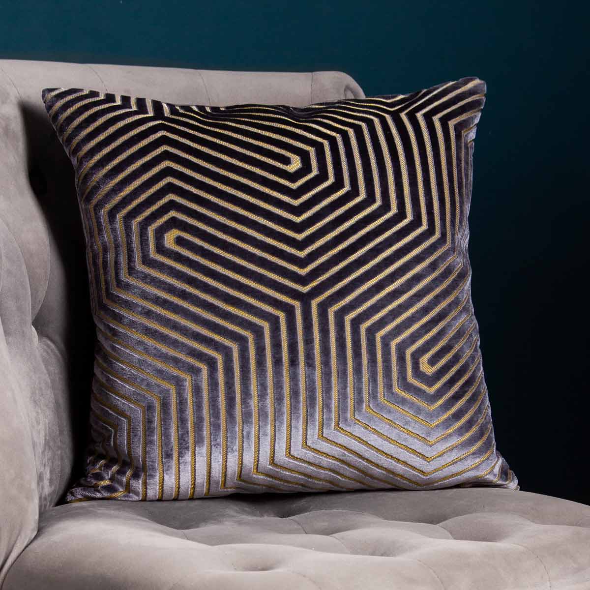 Charcoal geometric cut velvet cushion featuring a striking gold pattern, measuring 45cm x 45cm, placed on a soft, tufted gray sofa.