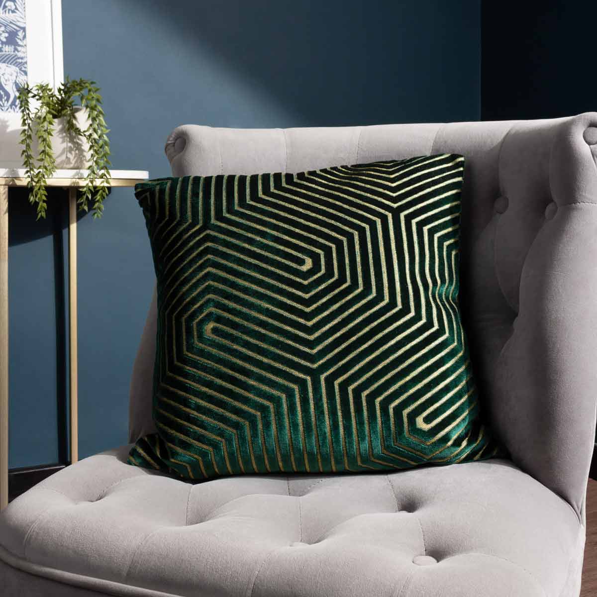 Emerald green geometric cut velvet cushion featuring intricate linear patterns, measuring 45cm x 45cm, placed on a light grey tufted chair.