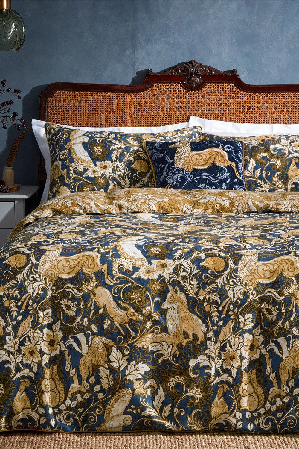 Premium cotton duvet cover set in blue featuring intricate floral and animal patterns, including hares, with coordinating pillowcases and a decorative cushion, suitable for a king-sized bed.