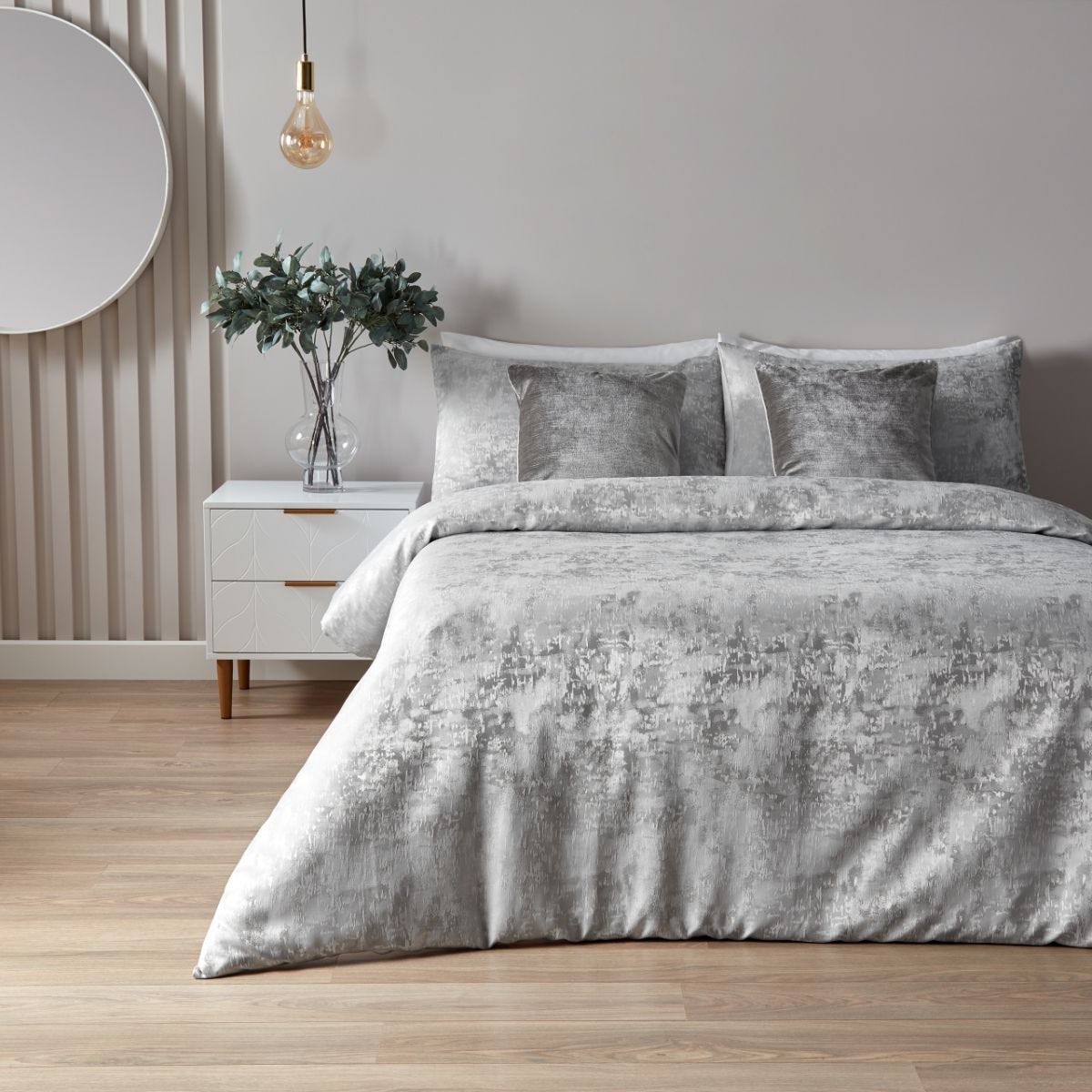 Silver cotton double duvet cover set by Paoletti, featuring a textured design, complemented by matching pillowcases, placed on a bed with a minimalist nightstand and decorative plant.