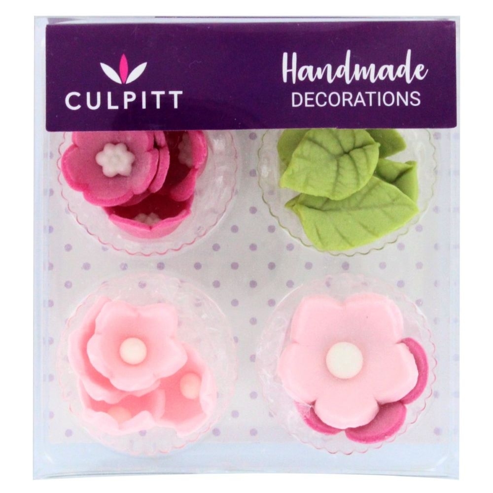 Sixteen pink flower and green leaf edible toppers in a clear plastic container, featuring various flower shapes with white centers and textured leaves, labeled "Handmade Decorations" by Culpitt.