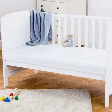 White cot with a pocket spring mattress, featuring a soft, quilted surface, accompanied by a blue blanket and a teddy bear on top, set on a wooden floor with colorful blocks nearby.