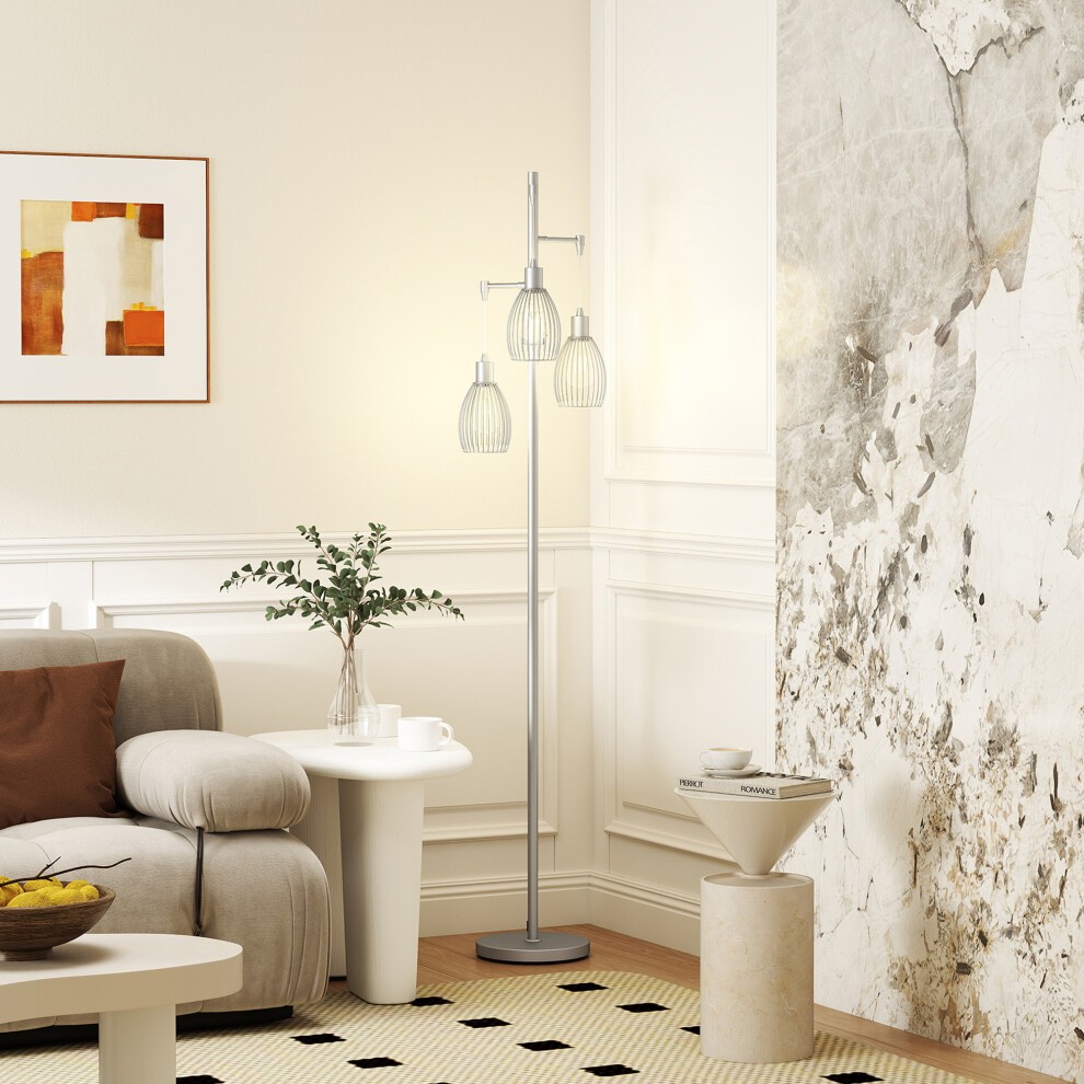 Three-light floor lamp with steel lampshades in silver, featuring a sleek industrial design, positioned beside a cozy sofa in a modern living room setting.