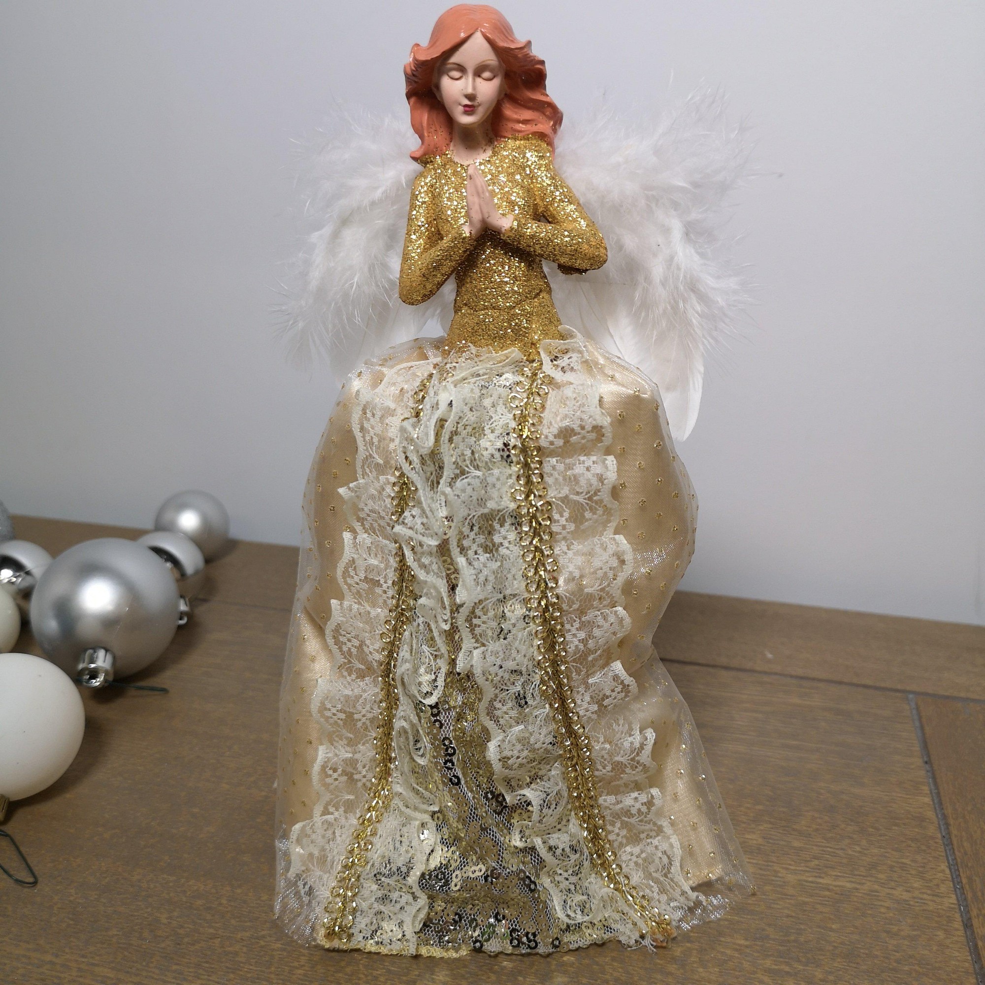 Gold angel tree topper with feather wings, wearing a glittery gown adorned with lace and sequins, features a serene expression and hands in prayer, perfect for Christmas decor.