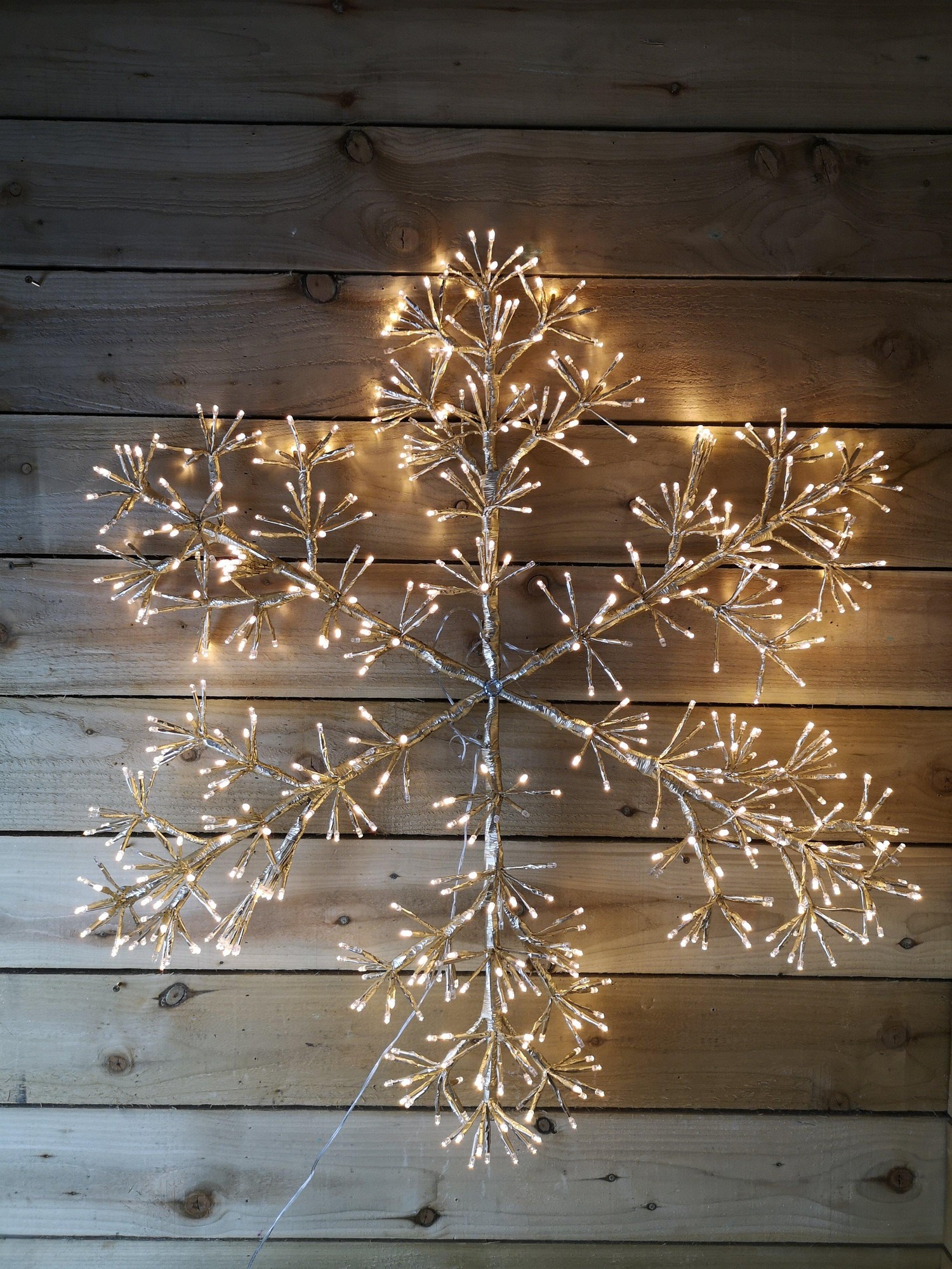 Gold starburst snowflake decoration featuring 660 warm white LEDs, with a metallic finish, designed for wall or window display against a rustic wooden background.