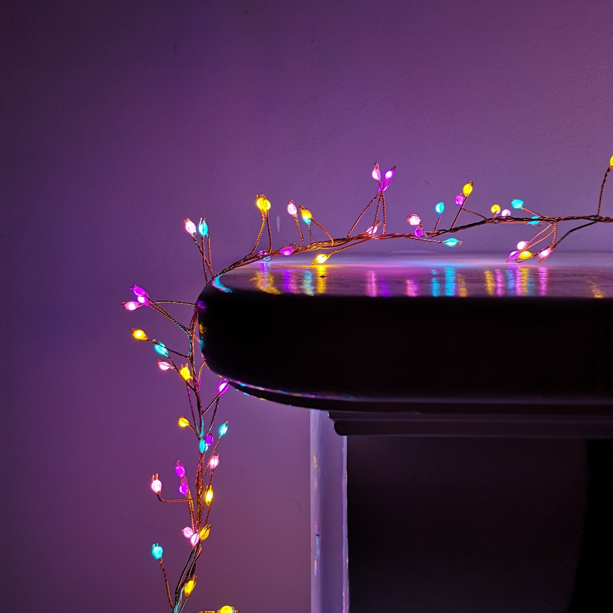 800 LED multifunction wire cluster lights in rainbow colors, featuring a timer, draped elegantly over a dark surface, showcasing vibrant pink, blue, yellow, and green bulbs.