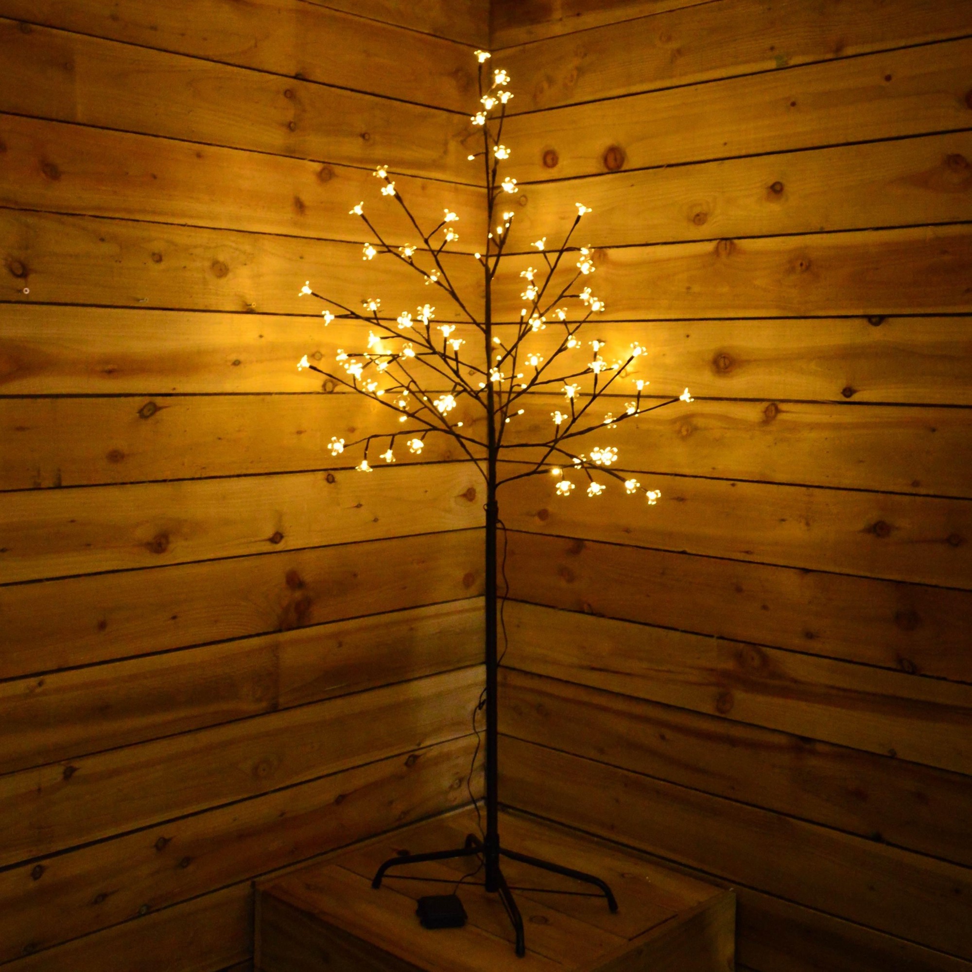 A 1.5m cherry blossom tree with 96 cool white LED lights, featuring delicate white flowers on dark branches, set against a rustic wooden backdrop.