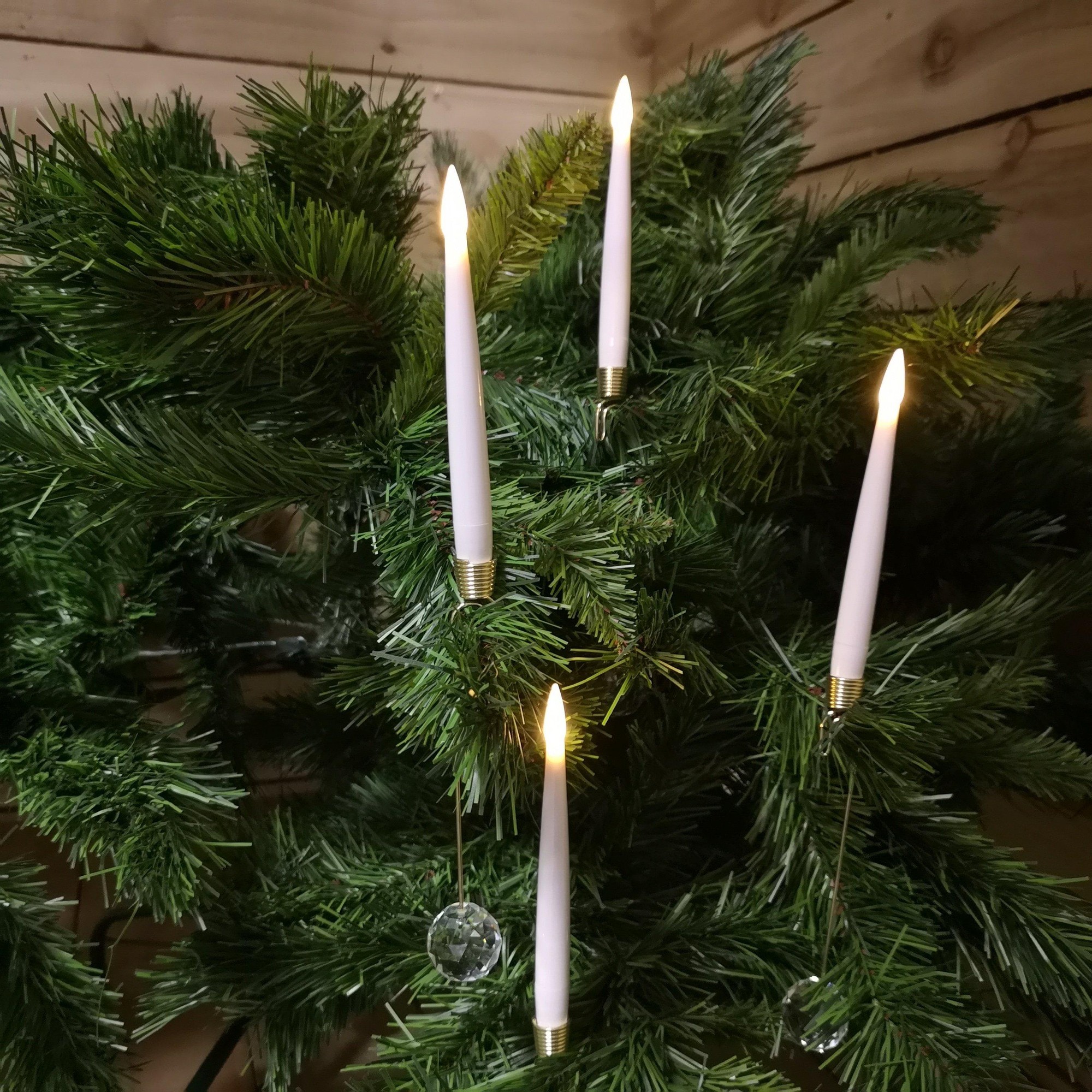 Warm white candle set featuring ten slender, white candles with gold holders, designed for indoor use, displayed among green faux pine branches. Remote control included.