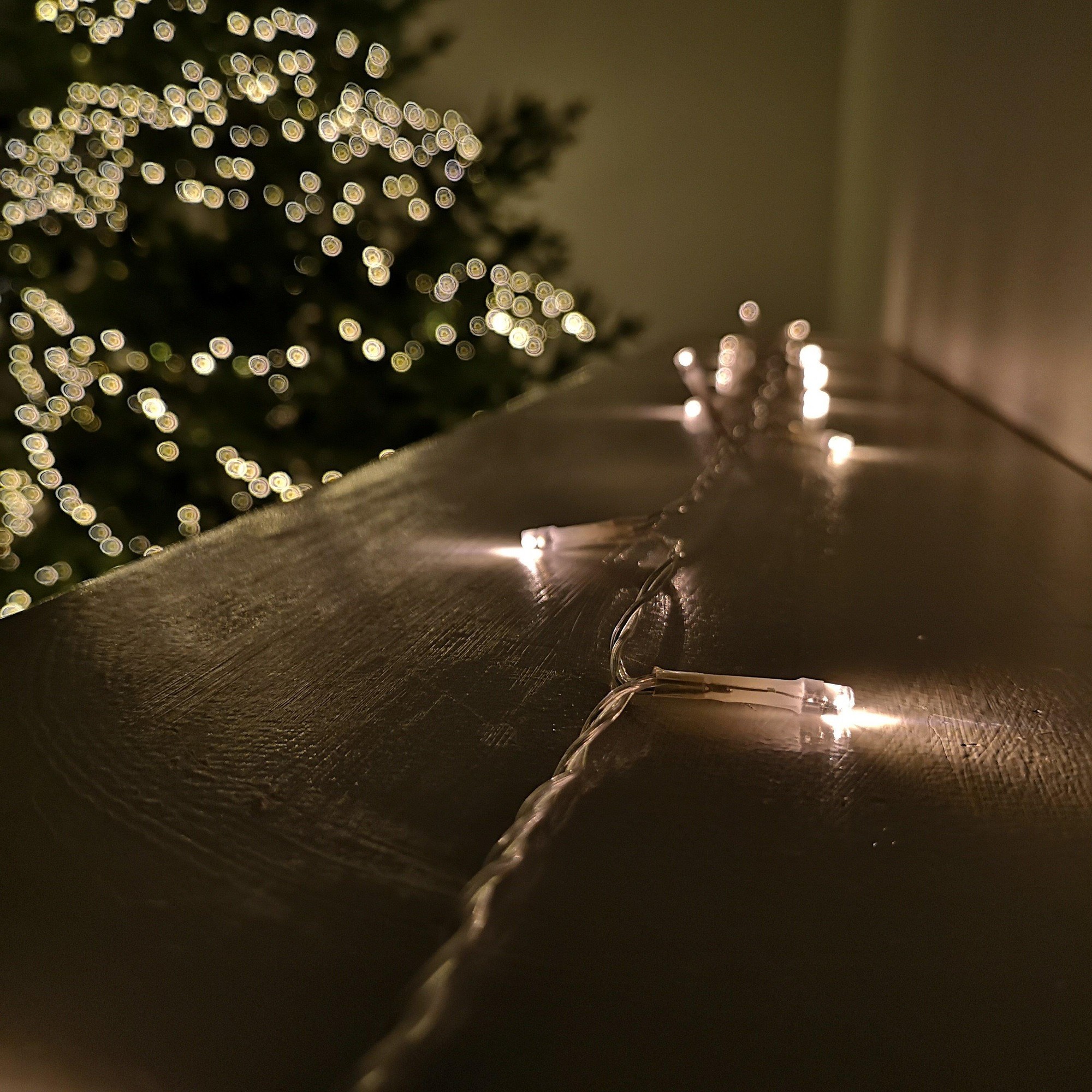 Warm white LED lights on a clear cable, with a timer function, arranged along a surface, softly glowing against a blurred background of a Christmas tree.