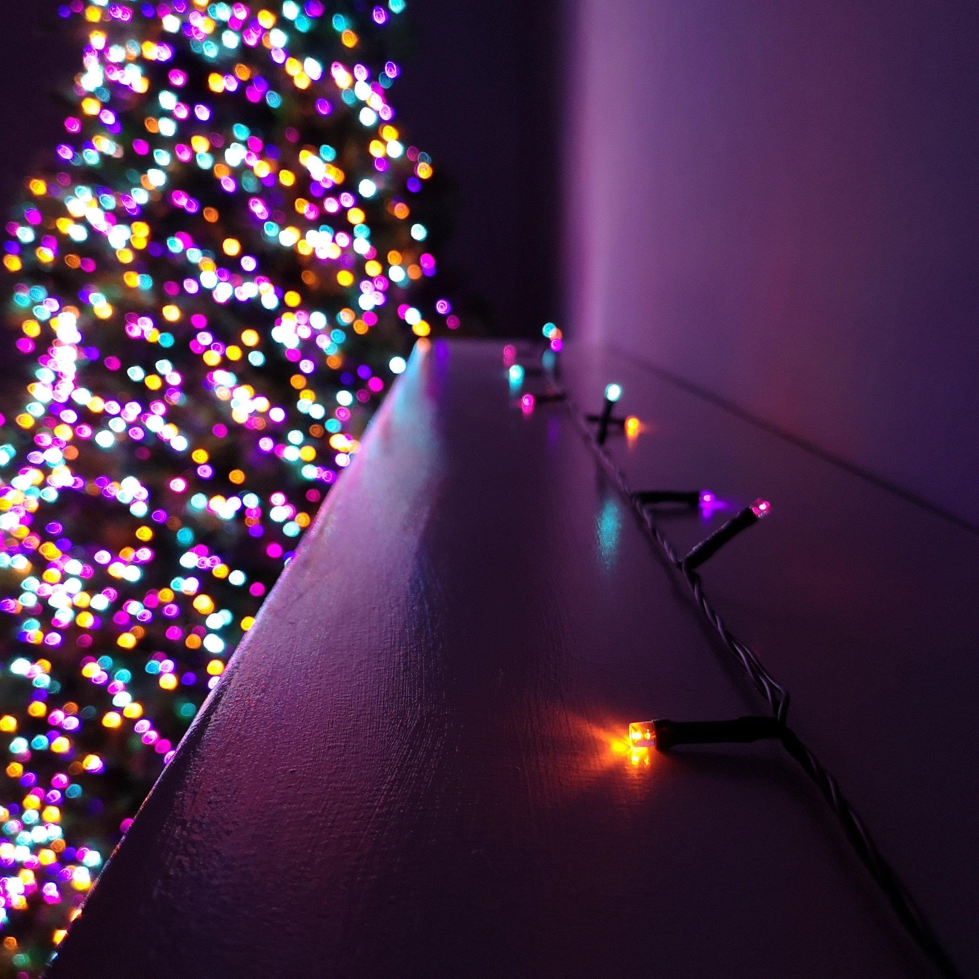 Colorful LED string lights with a black wire, featuring multi-function settings and a timer, displayed alongside a brightly lit rainbow Christmas tree.