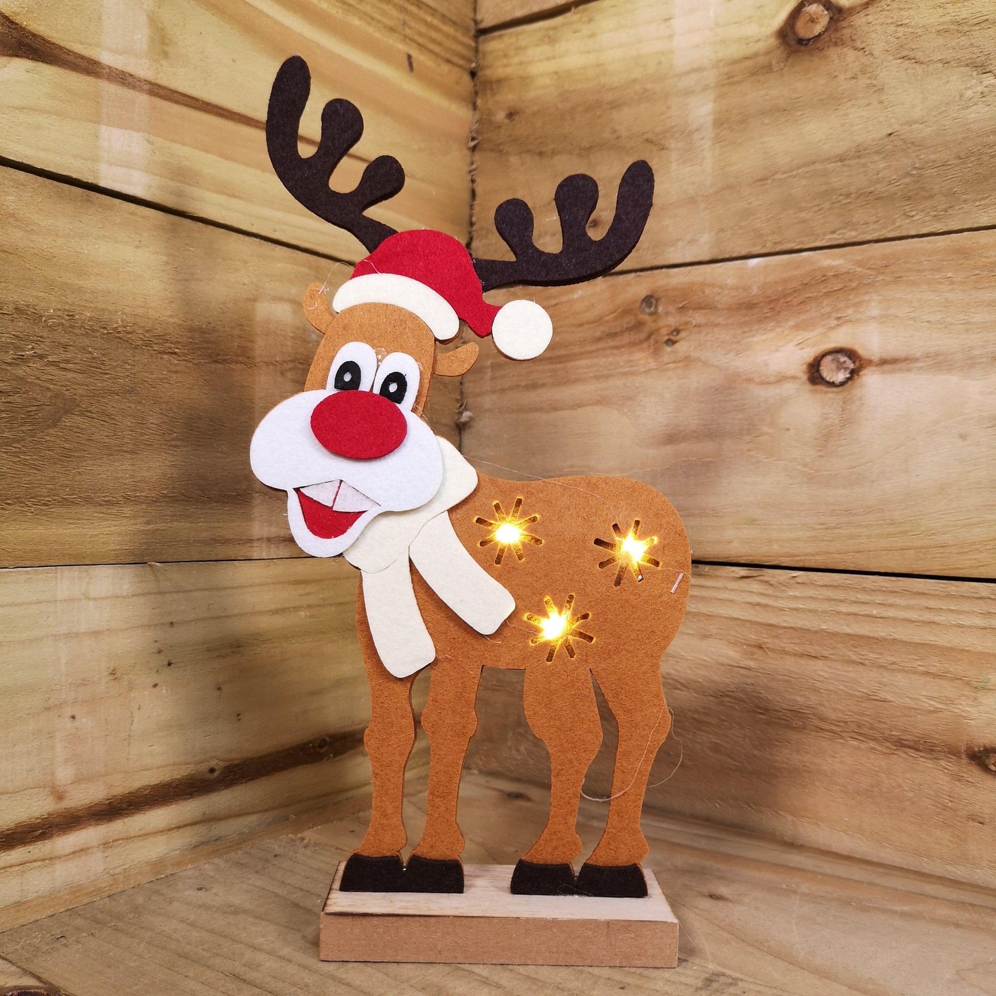Brown felt reindeer with a Santa hat, warm white LEDs, and a smiling face, featuring antlers and a scarf, standing on a wooden base against a rustic background.