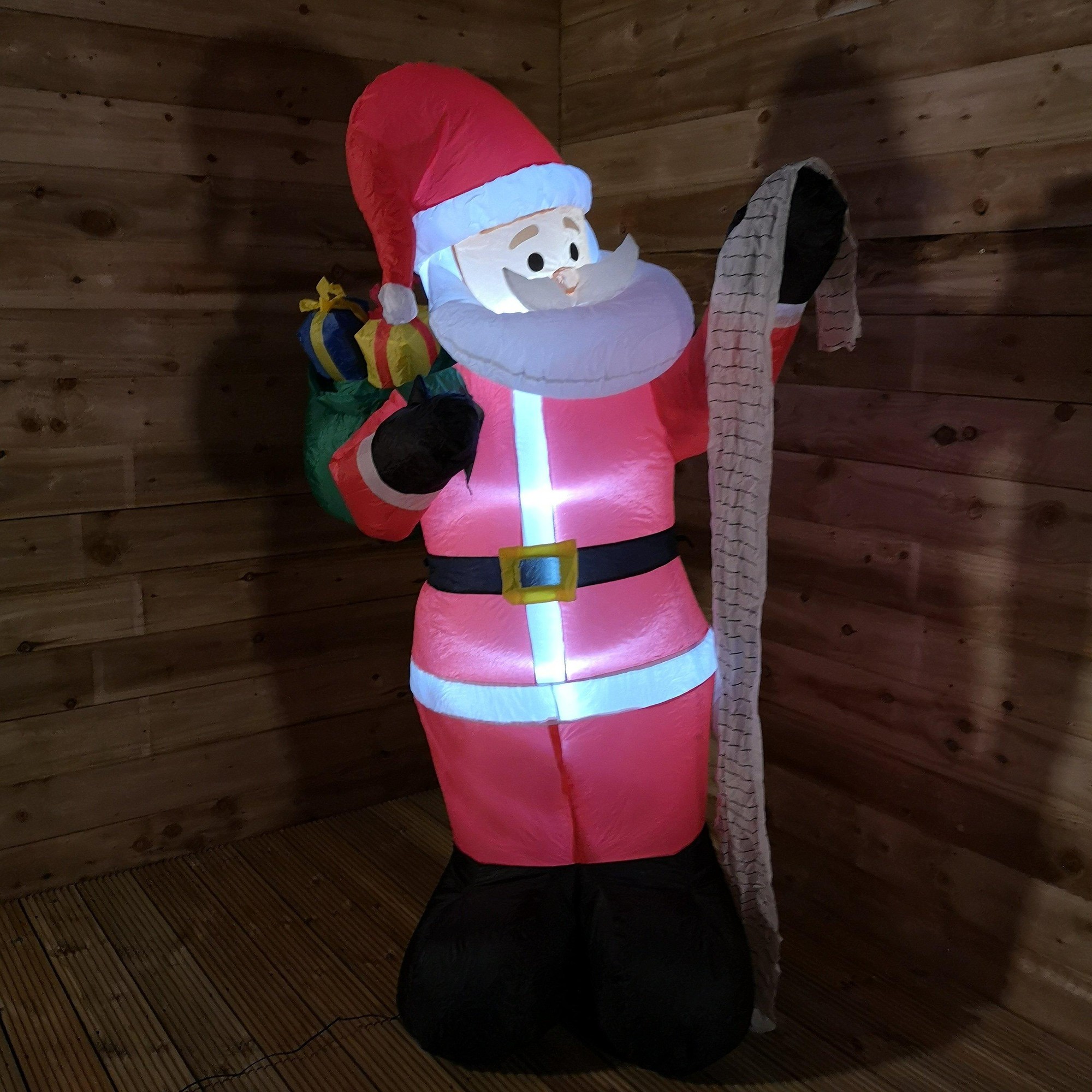 1.8M tall inflatable Santa in red suit holding a sack and a name list, featuring a cheerful face, white beard, and illuminated details, set against a wooden backdrop.