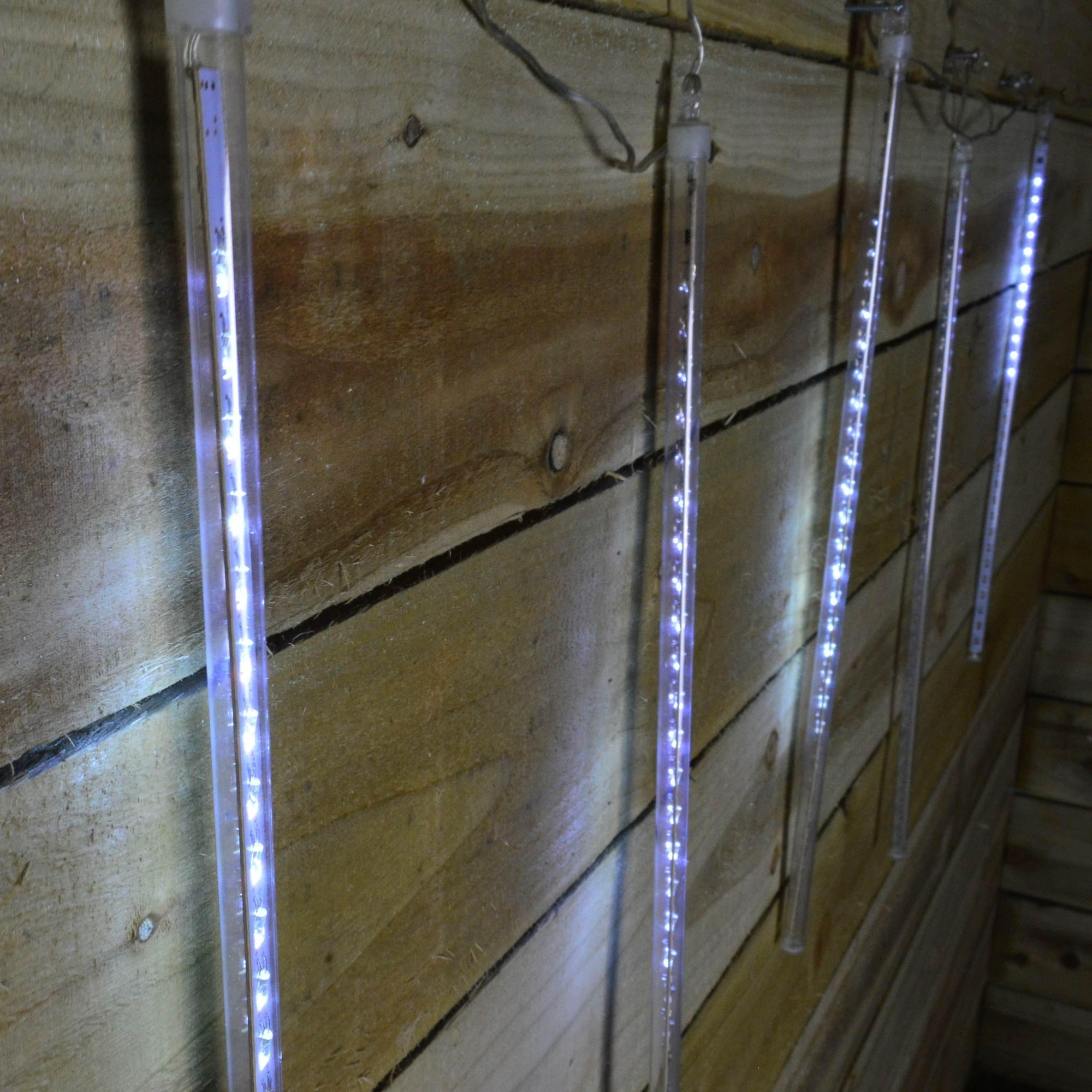 Bright white LED shower lights with a snowing effect, featuring five transparent tubes (50 cm each) hanging against a wooden backdrop.