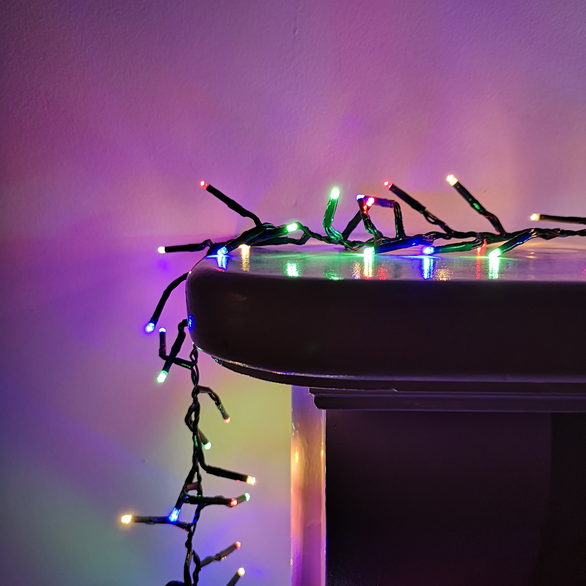 Multicoloured LED cluster lights with a black wire, showcasing green, red, blue, and yellow bulbs, draped over a dark surface, ideal for indoor and outdoor festive decoration.