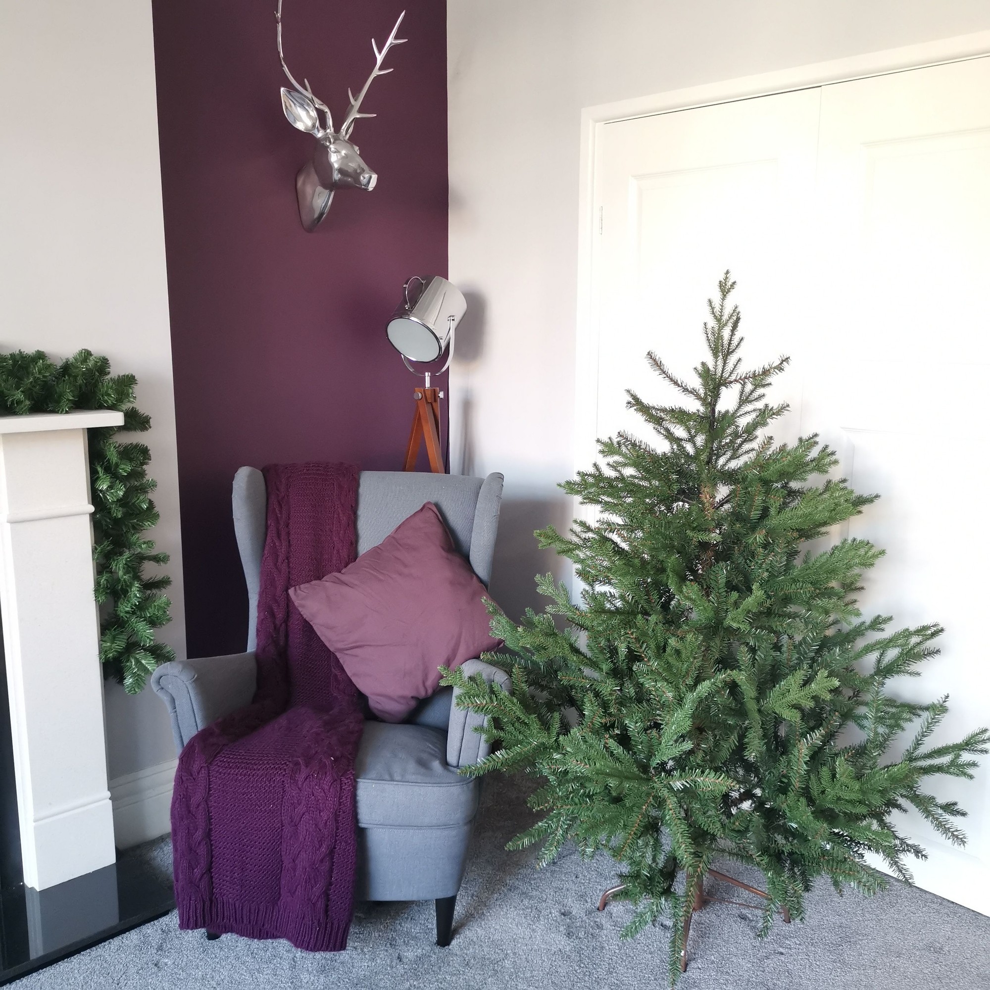 5ft Premier Christmas tree in Glenshee spruce style, featuring a natural green look with PE/PVC material, positioned beside a grey armchair with a purple throw and cushion.