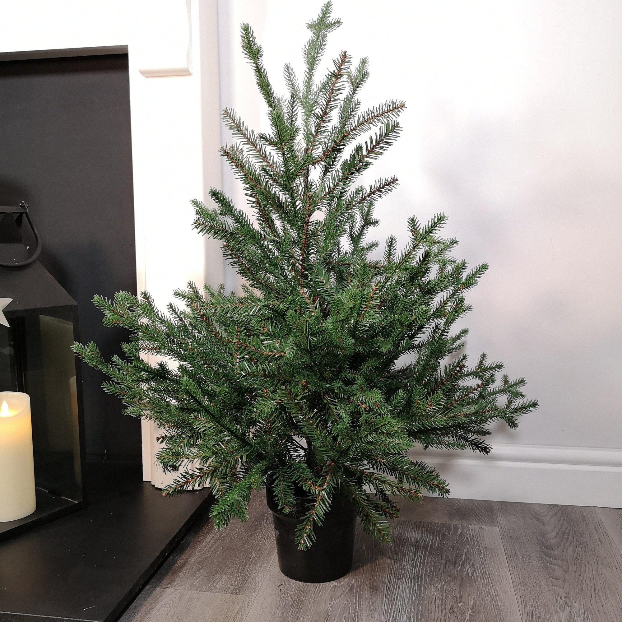 3ft green PVC Glenshee spruce Christmas tree with 537 tips, featuring a realistic design, set in a black pot, displayed near a fireplace with a candle.