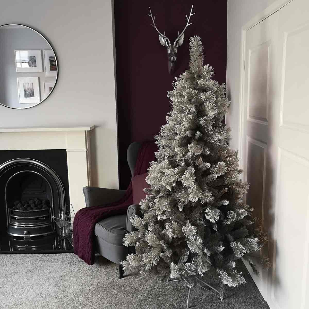 6ft grey PVC Christmas tree with 587 cashmere tips, featuring a full, snowy appearance, set in a cozy room with a fireplace and a dark accent wall.