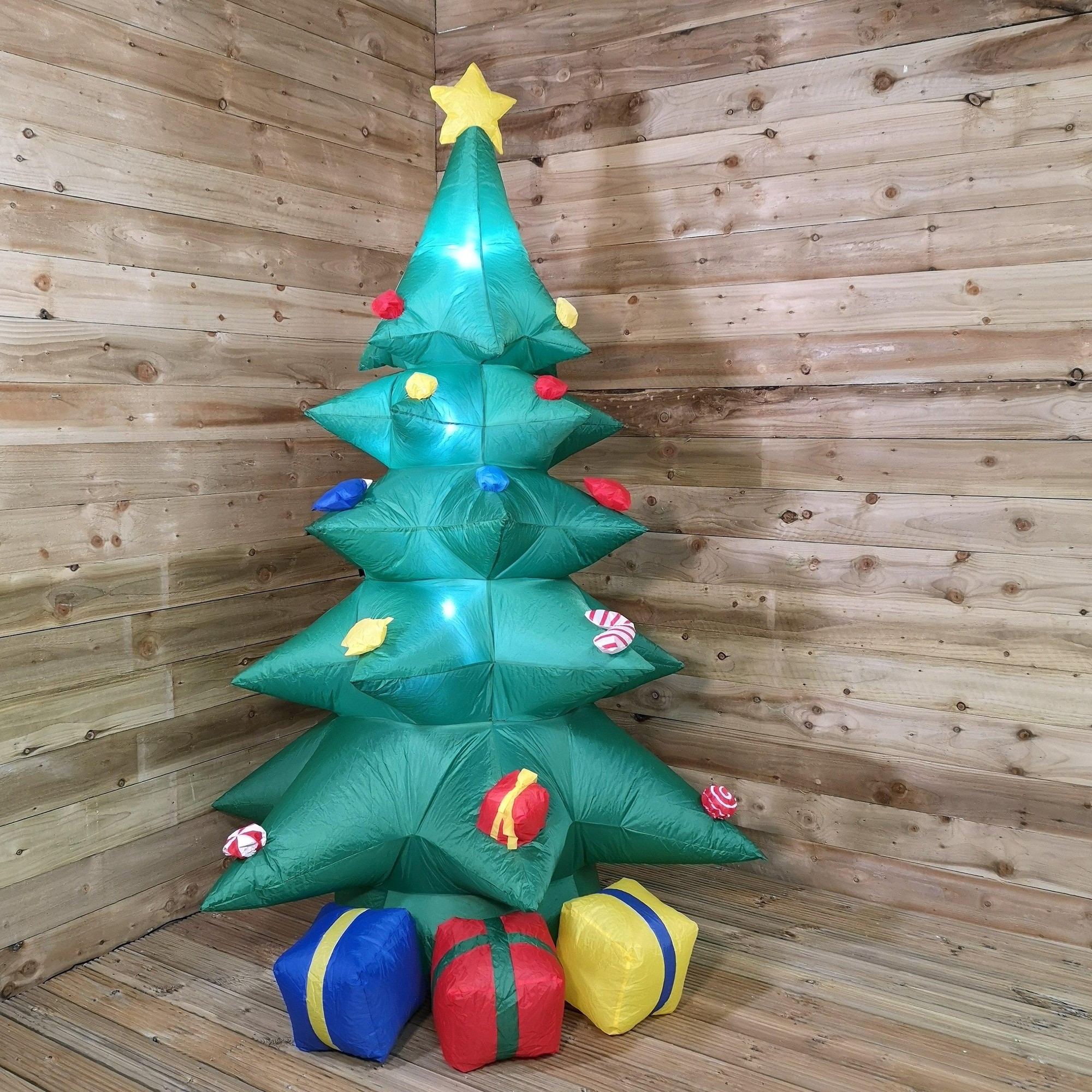 Inflatable green Christmas tree with colorful ornaments and a star on top, featuring three presents in red, yellow, and blue at the base, illuminated with LED lights.
